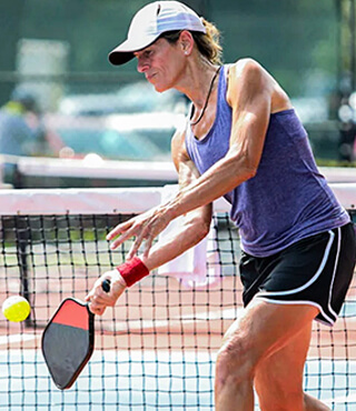 Woman in pickleball attire hitting a ball on a pickleball court during a match.